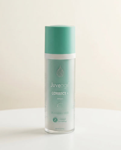 A bottle of Juveage Correct + Serum with a mint green cap and a frosted clear body, standing on a white surface against a warm off-white background.
